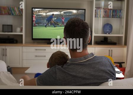 Vista posteriore di padre e figlio seduti a casa insieme partita di hockey in tv. Sport, competizione, intrattenimento e tecnologia concetto digitale composito i Foto Stock