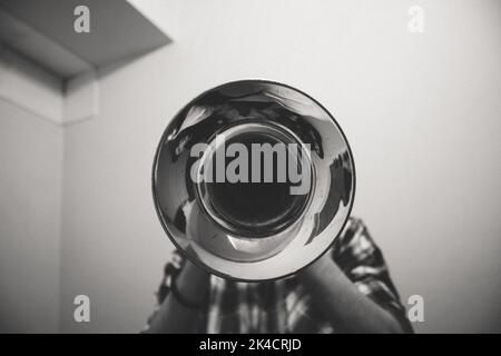 Un'immagine in scala di grigi di una persona che suona la tromba con il lato della campana rivolto verso la telecamera Foto Stock