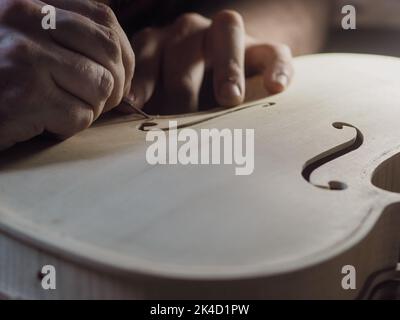 Primo piano di un maestro artigiano professionista luziatore scrupoloso lavoro dettagliato su violino in legno in un laboratorio. Foto Stock