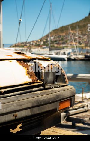 Uno scatto verticale di una vecchia auto arrugginita abbandonata danneggiata parcheggiata al porto di Hout Bay Foto Stock