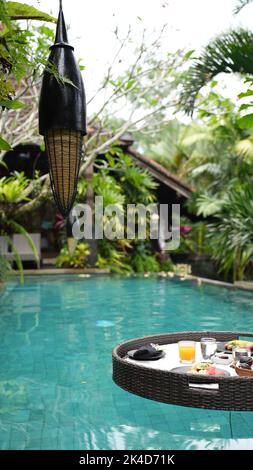 Uno shot verticale di un vassoio rotondo con cibo e bevande in piscina che galleggia sulla superficie dell'acqua. Foto Stock