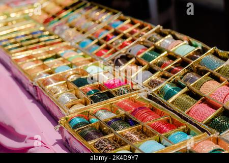 Un fornitore di bracciali che espone la sua collezione di bracciali in vetro e metallo molto colorati in un mercato aperto sulla strada Foto Stock