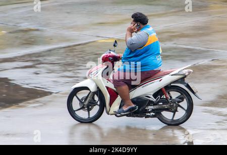 SAMUT PRAKAN, THAILANDIA, 26 2022 SETTEMBRE, Un autista moto taxi chiama dal telefono cellulare mentre si guida su strada bagnata Foto Stock