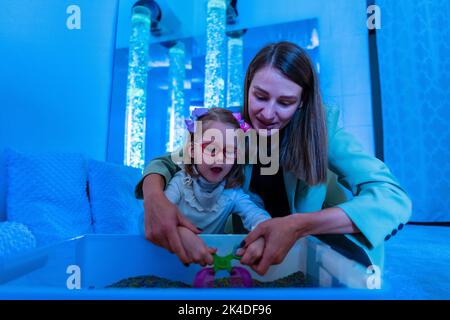 Bambino con disabilità fisica in sala stimolante sensoriale, snoezelen. Bambino che vive con la paralisi cerebrale interagendo con il suo terapeuta durante la terapia Foto Stock
