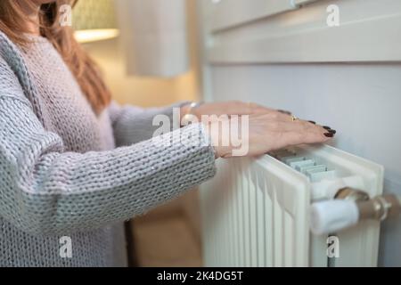 Donna che scalda le mani in un radiatore a causa del freddo dell'inverno. Foto Stock