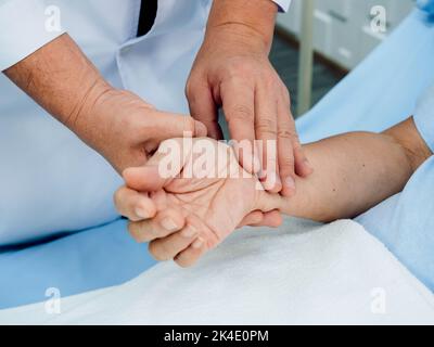 Primo piano la mano del medico nel camice di laboratorio bianco che tiene la mano del paziente anziano che si trova sul letto per controllare l'impulso del battito cardiaco da dita nel reco Foto Stock