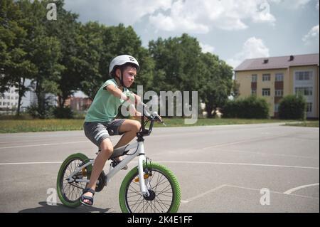 Ragazzo sportivo attivo con casco sportivo in bicicletta con sicurezza. Età della scuola caucasica pedalando sulla strada asfaltata della città Foto Stock