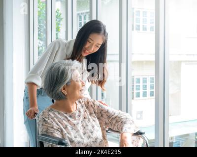 Donna anziana asiatica felice, madre o nonni su sedia a rotelle che si prendono cura da caregiver, sorridendo giovane donna, figlia o nipote che sostiene a h Foto Stock