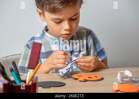 Preparazione di Halloween e decorazione domestica. Il ragazzo carino fa la decorazione con Halloween, ghirlande autunnali con le sue proprie mani. Foto Stock