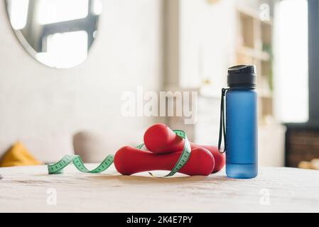 Set di manubri rossi, centimetri, attrezzature sportive, articoli per il fitness, una bottiglia di buoi sul tavolo Foto Stock