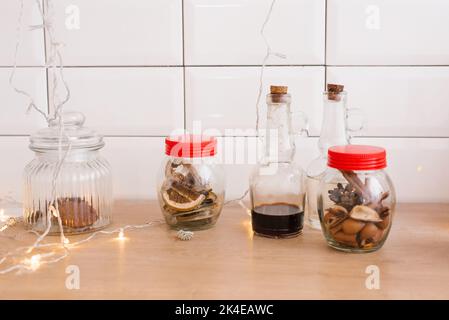 Vasetti di vetro di frutta secca, salsa in bottiglia e luci di Natale in una cucina scandinava Foto Stock