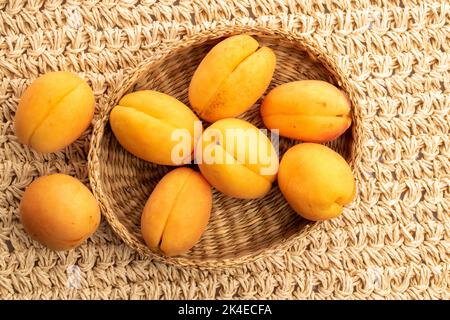 Diverse albicocche di ananas gialle in un piatto di paglia, macro, su un tappetino di paglia, vista dall'alto. Foto Stock