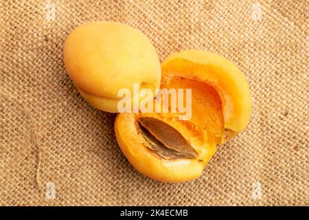 Un'albicocca intera e un'albicocca di ananas tagliata a metà, macro, su tessuto di iuta, vista dall'alto. Foto Stock