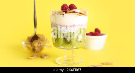Bicchiere di delizioso budino di chia con frutta su sfondo giallo Foto Stock