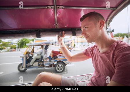 Uomo che si gode un giro in tuk tuk durante la giornata di sole. Ritratto del turista in taxi. Bagkok, Thailandia Foto Stock