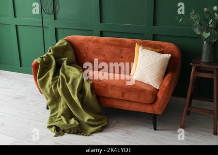 Divano rosso con plaid e cuscini vicino alla parete verde Foto Stock