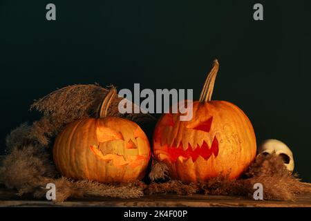 Zucche di Halloween intagliate con erba di pampas e cranio sul tavolo su sfondo nero Foto Stock