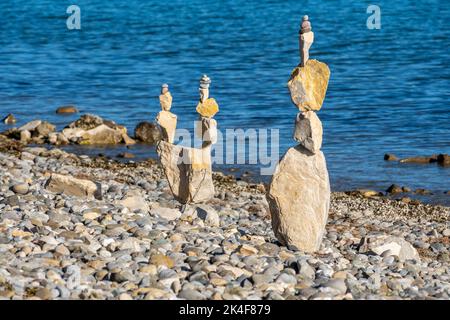 Piramidi di pietra sulla riva del lago con vista sulle montagne e cielo azzurro soleggiato Foto Stock