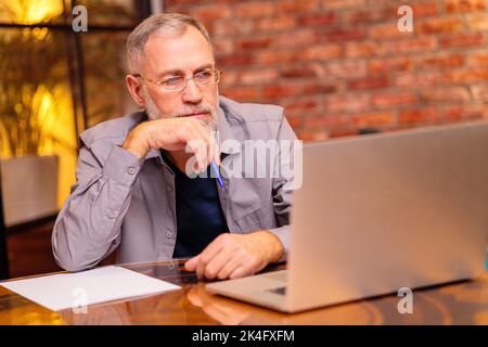 l'uomo anziano preoccupato siede vicino al laptop e prova faccia il pagamento in linea Foto Stock