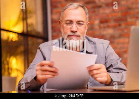 l'uomo anziano preoccupato siede vicino al laptop e prova faccia il pagamento in linea Foto Stock