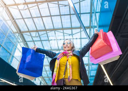 Donna anziana felice con borse di shopping sorridente durante le feste salse di festa. Donna che celebra eccitato. Foto Stock