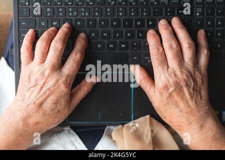 Donna anziana che digita sulla tastiera del notebook. Vista dall'alto Foto Stock