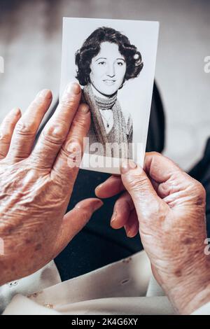 CIRCA 1970: Donna anziana mani in possesso di vintage, foto in bianco e nero della giovane donna. Il concetto di passare del tempo Foto Stock