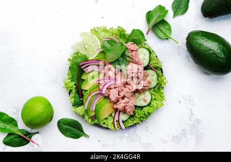 Insalata di tonno con avocado, cetriolo, cipolla rossa e lattuga. Sfondo in pietra bianca, vista dall'alto, spazio copia Foto Stock