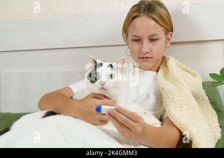 La ragazza malata guarda il termometro, accanto a lei è un gatto. Il concetto di salute e medicina. Foto Stock