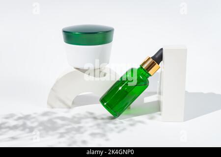 Set di bottiglie di vetro verde per cosmetici e vasetto crema sul podio bianco. Sfondo mockup con figure geometriche cocncrete e spazio copia. Scendi con Foto Stock