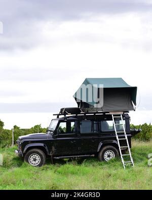 Furgone fuoristrada parcheggiato in un campo con tenda sul tetto. Foto Stock