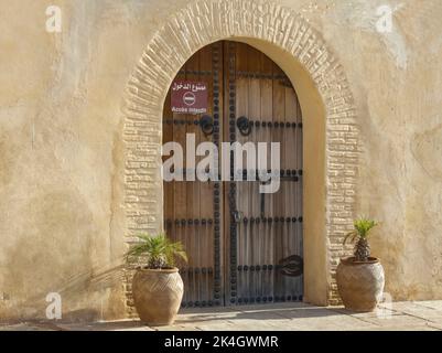 Parete di colore pallido con porta ad arco e porte in legno con borchie, cerniere e maniglie in metallo nero Foto Stock