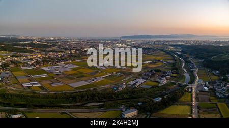 Vista aerea panoramica delle fattorie costiere e delle luci dalla città al tramonto Foto Stock