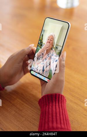 Le mani di una donna che effettua una videochiamata natalizia con una donna caucasica anziana che soffia il bacio. natale, festa e tecnologia di comunicazione. Foto Stock