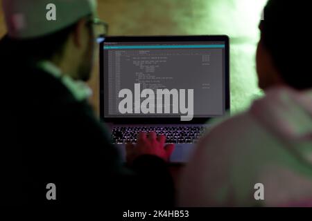 Vista posteriore di due diversi colleghi maschi che utilizzano un computer portatile con codifica sullo schermo. Codifica, programmazione e computer tecnologia immagine composita digitale. Foto Stock