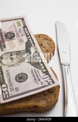 Banconota da 50 dollari sulla fetta di pane marrone accanto al coltello in acciaio inossidabile. Foto Stock