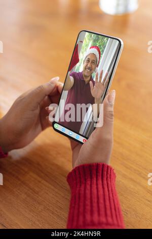 Le mani di una donna che effettua una videochiamata natalizia con un uomo biraciale anziano sorridente a santa Hat. natale, festa e tecnologia di comunicazione Foto Stock