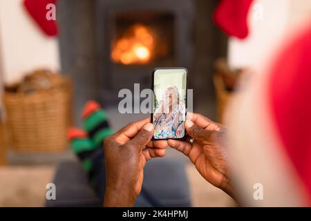 Afro americano uomo fare smartphone video chiamata di natale con donna caucasica anziana soffiare bacio. natale, festa e comunicazione technolog Foto Stock