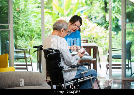 Pillole di infermiera della giovane donna asiatica con aiuto prescrive la medicina al paziente più anziano disabile su sedia a rotelle quando il paziente anziano dell'uomo anziano è tempo di andare a casa Foto Stock