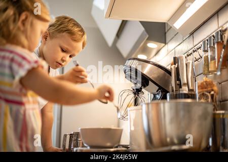 Madre che si prende cura di cucinare con figlia e figlio insieme la famiglia che prepara i waffle mescolando l'impasto Foto Stock