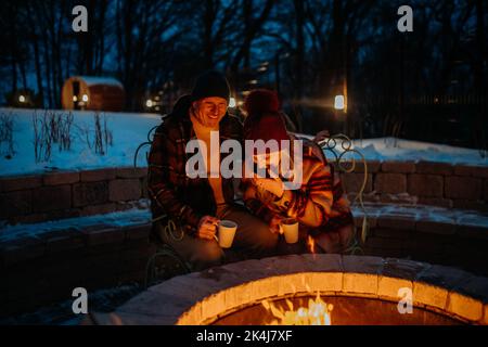 Coppia anziana seduta e riscaldamento insieme al caminetto all'aperto nella sera d'inverno. Foto Stock