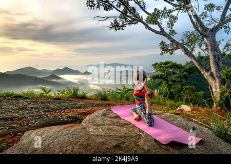 Nha Trang City, Vietnam - 23 agosto 2022: Una donna anziana pratica i movimenti di Yoga al mattino sulle montagne di Nha Trang. Guardando fuori in th Foto Stock