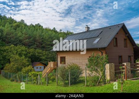 Casa in legno con pannelli solari installati. Energia alternativa, risparmio di risorse e concetto di stile di vita sostenibile. Foto Stock