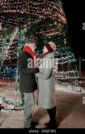 Coppia anziana innamorata in piedi di fronte alle decorazioni festive Foto Stock