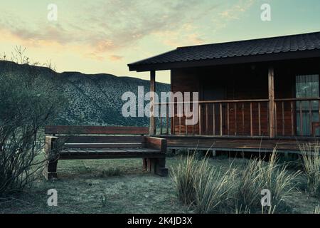 Solitaria capanna rurale e panca nella steppa con le montagne. Concetto di solitudine nella natura e nell'architettura Foto Stock