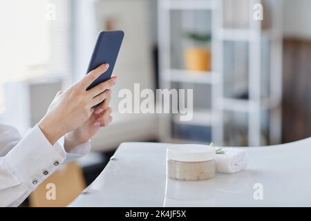 Minimal closeup di giovane donna che prende le immagini del prodotto di creme di bellezza fatte a mano e sali di SPA con smartphone Foto Stock