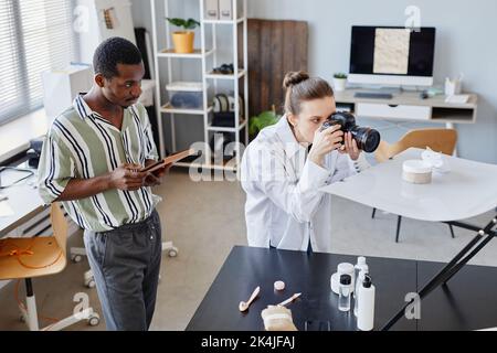 Ritratto ad angolo alto di due fotografi che scattano immagini di prodotti con una fotocamera professionale in studio Foto Stock