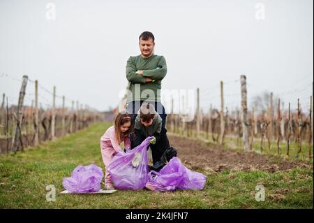 Famiglia con sacco rifiuti raccolta rifiuti mentre la pulizia nei vigneti . Conservazione ambientale ed ecologia, riciclaggio. Foto Stock