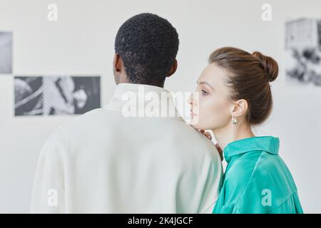 Vista posteriore minima di una giovane coppia che guarda la galleria fotografica nel museo insieme a una donna che riposa la testa sulla spalla dei boyfriends, spazio copia Foto Stock