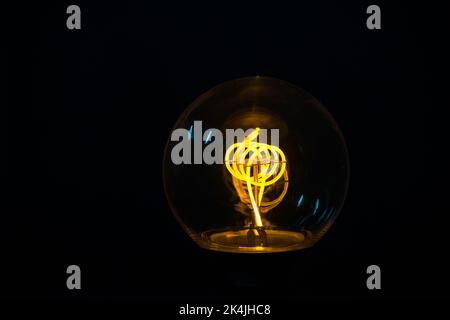 Una classica lampadina Edison su sfondo nero con spazio per il testo. Lampadina illuminata su sfondo nero Foto Stock
